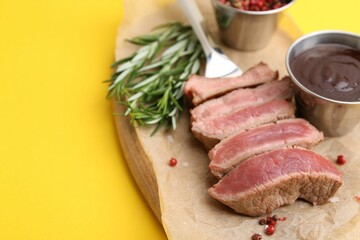 Delicious sliced beef tenderloin with different degrees of doneness, sauce and spices on yellow table, closeup. Space for text