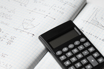 Copybook with handwritten maths formulas and calculator as background, closeup