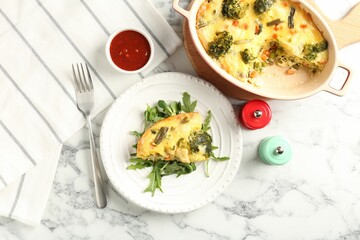 Tasty vegetable casserole, arugula, shakers, sauce and fork on white marble table, flat lay