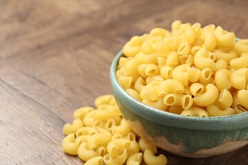 Raw horns pasta in bowl on wooden table, closeup. Space for text