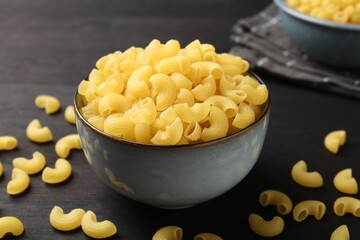 Raw horns pasta in bowl on dark wooden table, closeup