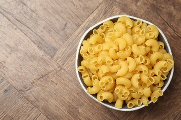 Raw horns pasta in bowl on wooden table, top view. Space for text