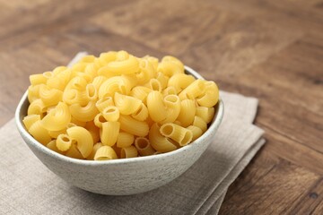 Raw horns pasta in bowl on wooden table, closeup