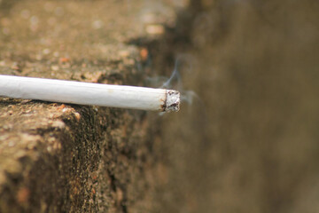 Lit white cigarette with smoke coming out of it sitting on the grey city concrete with copy space	
