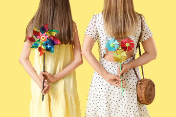 Teenage girl and her mother with toy windmills on yellow background, back view