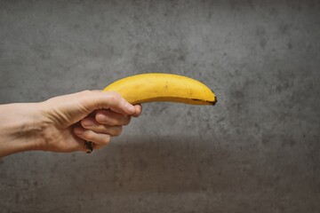 Straight Arm Holding Banana Like a Gun Against Gray Wall