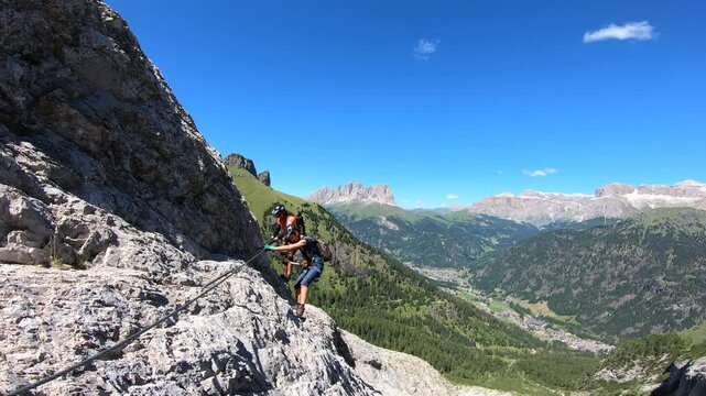 Couple climbing Via Ferrata dei Finanzieri on Colac overlooking the Sella Group and Sassolungo in the Dolomites, Italy
