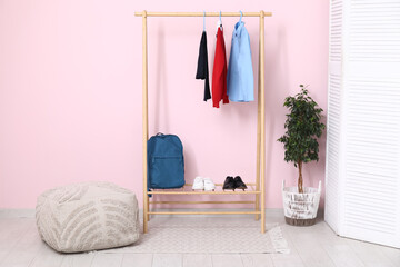 Rack with stylish school uniform, backpack, houseplant and pouf near pink wall in room