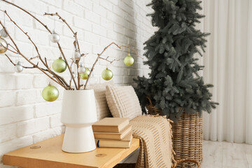 Vase with tree branches and Christmas baubles on wooden bench near white brick wall