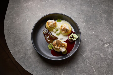 Elegant dessert with meringue, grapes, cream, garnished with flower on black plate over marble table culinary art concept