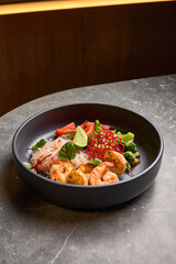 Delicious shrimp with fresh lime, vibrant vegetables, rice noodles served in a stylish black bowl on grey stone table, Asian cuisine concept