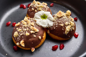 Delicious chocolate covered donuts with crushed nuts and delicate flower topping, surrounded by vibrant pomegranate seeds, dessert concept