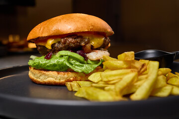 Juicy beef burger with melted cheese, fresh lettuce and crispy fries on a plate ready to eat delicious food concept