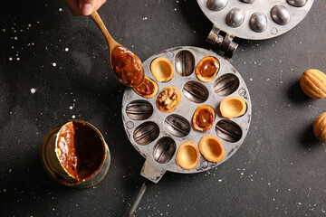 Woman cooking tasty walnut shaped cookies with boiled condensed milk on dark background