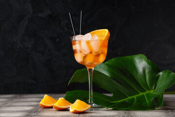 Glass of Aperol spritz cocktail and palm leaf on grey tile table