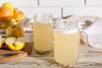 Mason jars of fresh apple kvass and fruits on white wooden table