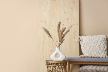 Vase with pampas grass and soft bench near beige wall in room