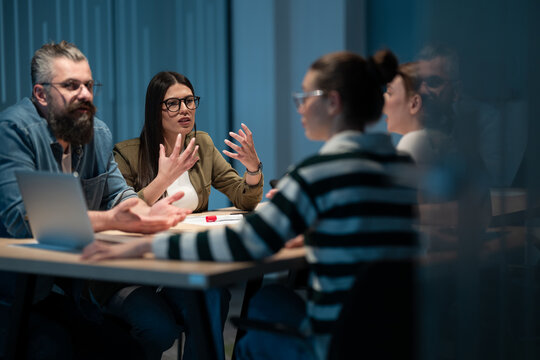A diverse team of young professionals collaborates in a modern office conference room. Businesspeople discuss strategy, technology, and planning, using laptops to develop an innovative e-commerce