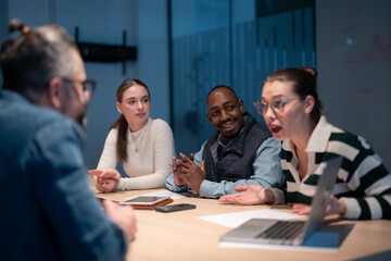 A diverse team of young professionals collaborates in a modern office conference room. Businesspeople discuss strategy, technology, and planning, using laptops to develop an innovative e-commerce