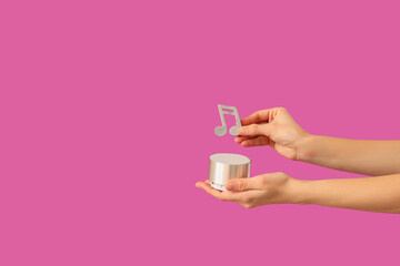 Female hands holding wireless speaker and music note on pink background