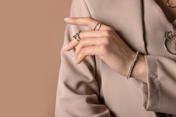 Pretty young woman in stylish blazer with silver rings, bracelet and necklace on beige background, closeup