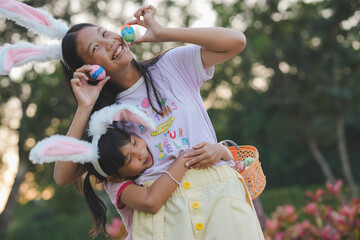 Obraz premium Two girls have fun finding Easter eggs a favorite activity for all kids. The girls wear cute bunny ears on the head holding a basket with Easter eggs in a natural garden with evening light.