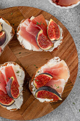 Bruschetta or toast with goat cheese spread, prosciutto, figs and honey on a board.