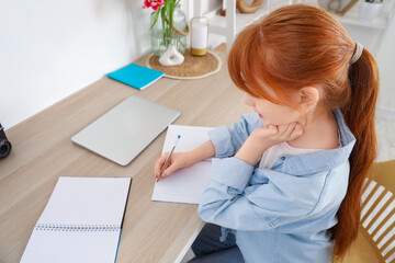 Cute redhead girl doing homework at home