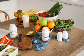 Fresh vegetables, fruits, vitamins and measuring tape on table in kitchen, closeup. Healthy food...
