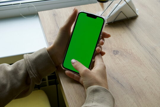 A person holds a smartphone with a green screen, ideal for mockups and customizable content.