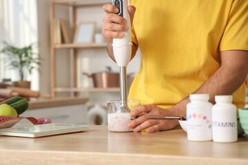 Young man with blender making healthy smoothie from fresh vegetables in kitchen, closeup. Healthy food concept