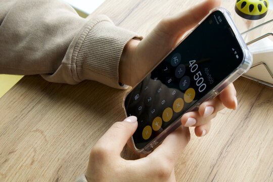 A person is using the Calculator app on an iPhone. The phone is held in one hand.