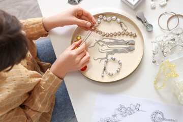 Young female jewelry designer making bracelet on table, top view