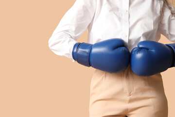 Young businesswoman with boxing gloves on beige background, closeup. Knockout concept