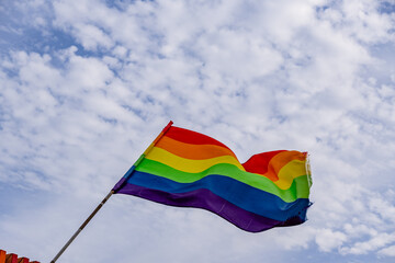 A rainbow flag is flying in the sky on a cloudy day