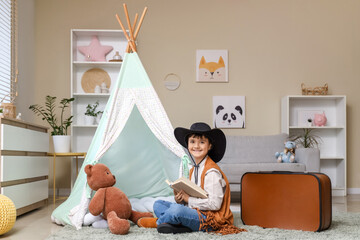Cute boy dressed as cowboy reading adventure book at home