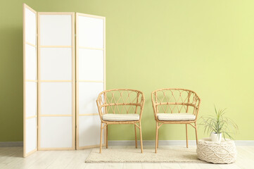 Wicker chairs, houseplant on pouf and folding screen near green wall in room