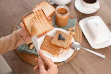Young woman spreading peanut butter on toast with knife in kitchen, closeup