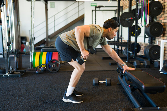 Determined sportsman doing single-arm dumbbell rows in a modern gym, focusing on building strength and muscle mass