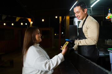 Smiling customer paying digitally for savory street food beside illuminated food truck during nighttime urban scene