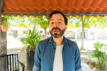 Relaxed hispanic man whistling cheerfully, standing amid lush garden greenery under warm sunlight