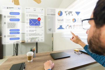 Point of view of a man wearing AR glasses pointing at holographic screen with data, charts and emails, using mixed reality technology in office