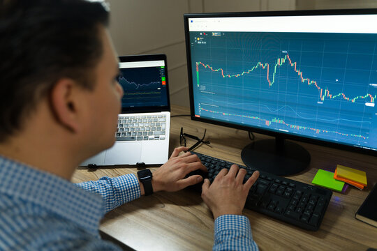 Professional trader reviewing financial charts across multiple screens, working from home trading workspace
