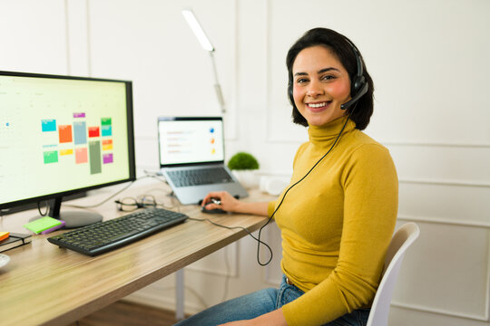 Latin virtual assistant with a headset multitasking on computer and laptop, managing tasks efficiently in a modern home office setup