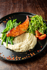 A beautifully plated dish featuring grilled salmon, sautéed green beans, creamy mashed potatoes, and fresh salad with cherry tomatoes, garnished with herbs and spices.
