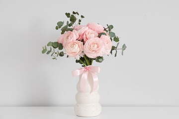 Vase with bouquet of beautiful ranunculus flowers on table near white wall, closeup