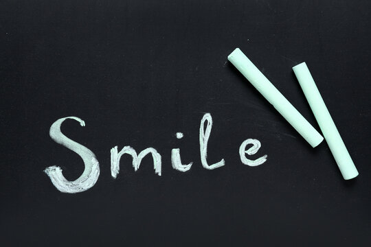 Green chalks with drawn word SMILE on blackboard - Powered by Adobe
