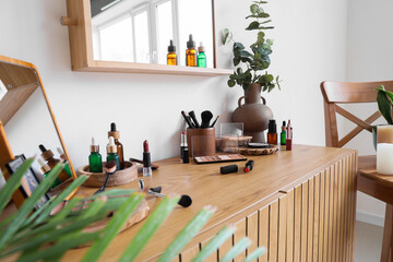 Vase with eucalyptus, mirror and makeup products on table in light room