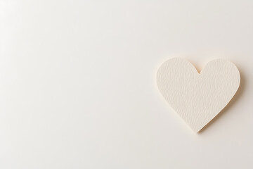 Fototapeta premium A cream-colored paper heart lies on a smooth, minimalist off-white surface, symbolizing love and affection. The heart is textured, adding a touch of subtle detail.