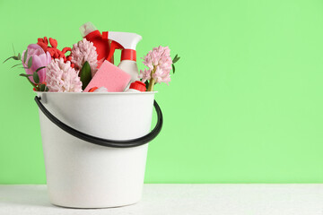 Cleaning supplies with spring flowers on table against green background